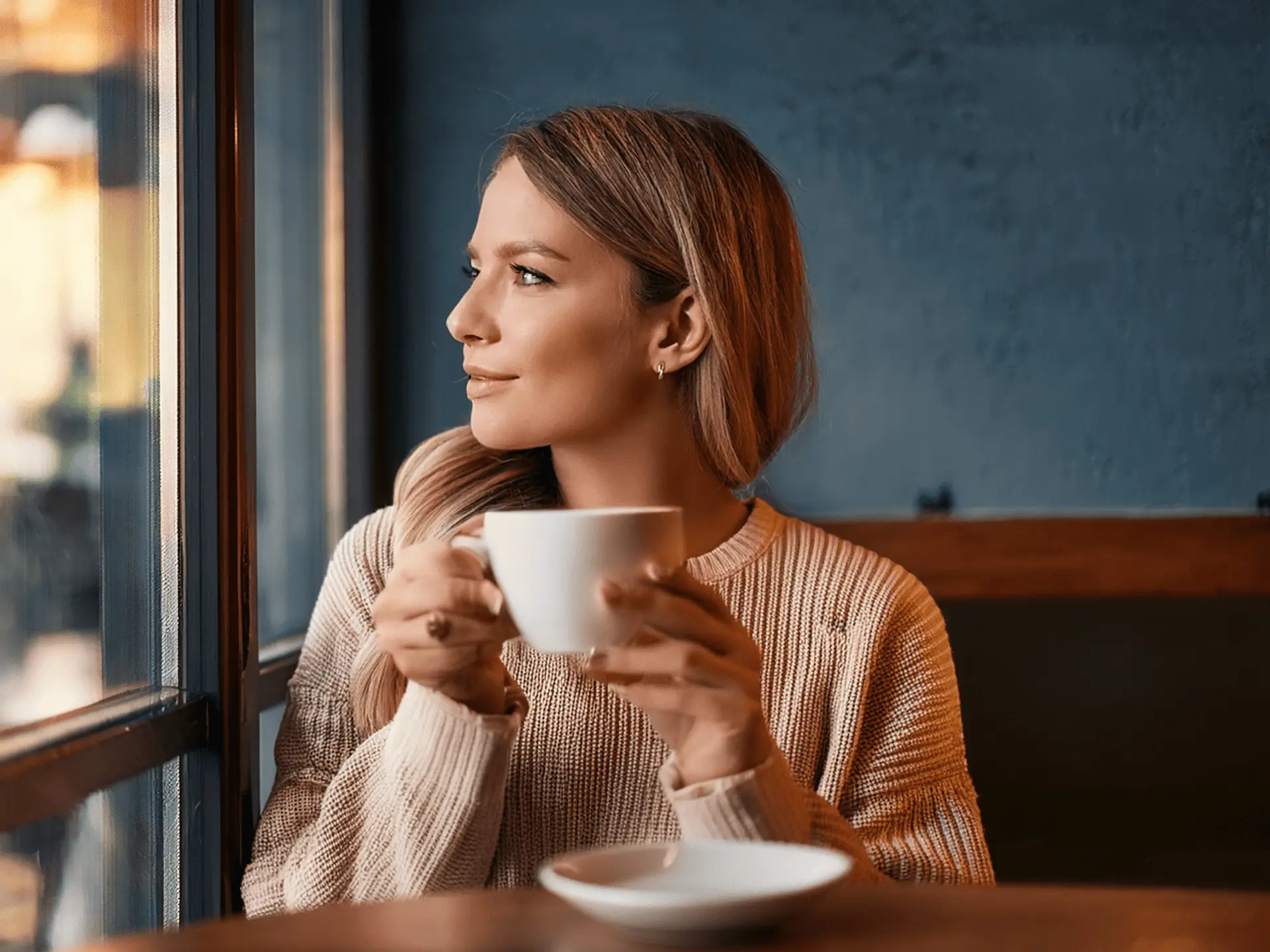 Ženska uživa kavo ob oknu v prijetnem ambientu